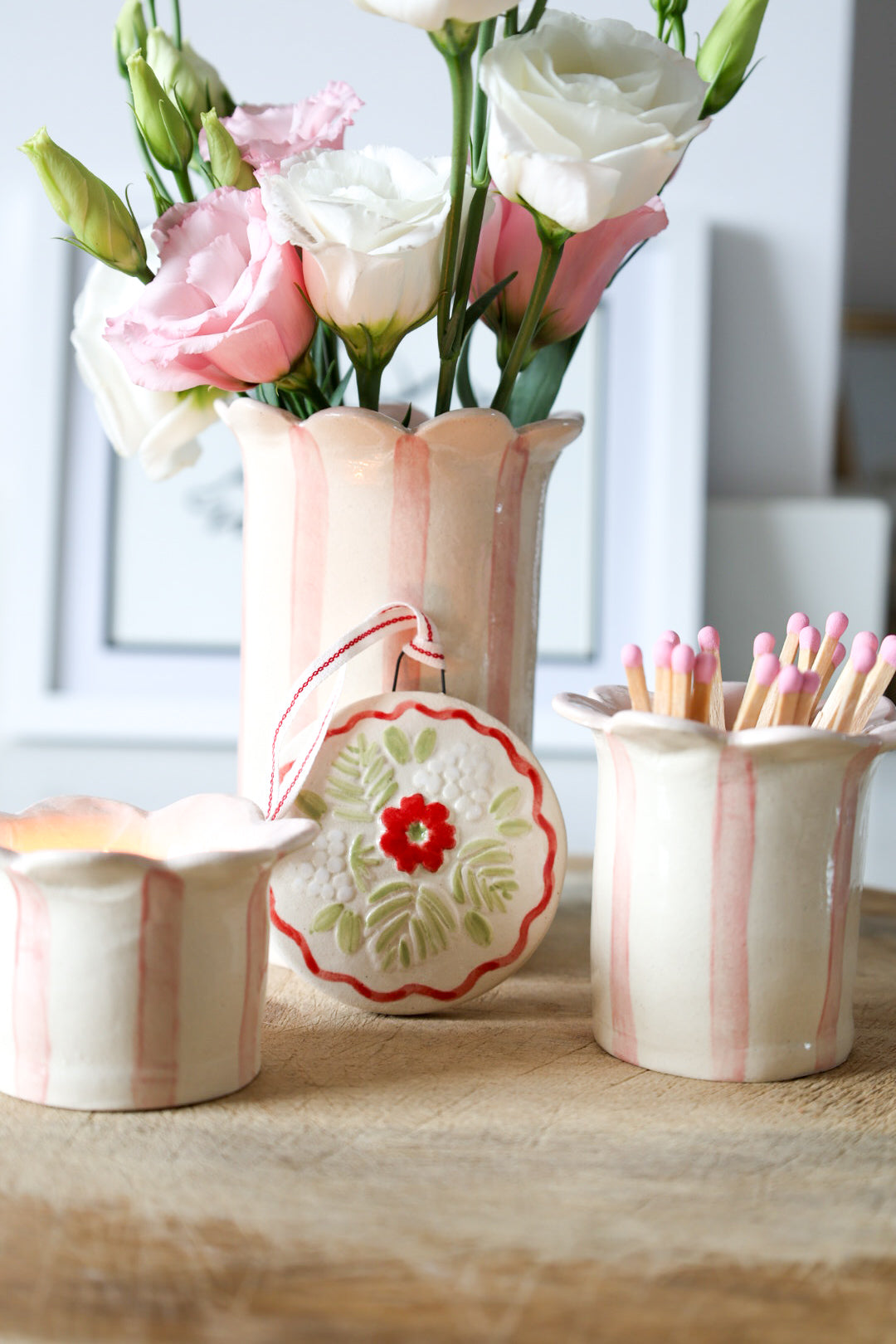 Decorative ceramic Christmas hanger surrounded by a vase with flowers, a tea-light holder and a match striker on a wooden surface. All made by Sea Bramble Ceramics