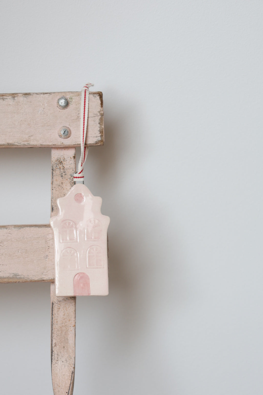 Small pink Nordic house Christmas tree ornament, handmade by Sea Bramble Ceramics, hanging on a wooden chair against a light grey background