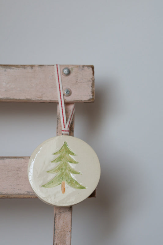 Decorative round ornament with a green tree design on a wooden stand against a plain background. Handmade by Sea Bramble Ceramics.