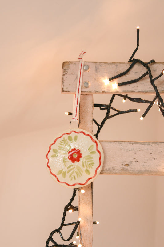 Decorative Christmas tree decoration with floral design hanging on a wooden board with Christmas lights.Handmade by Sea Bramble Ceramics.