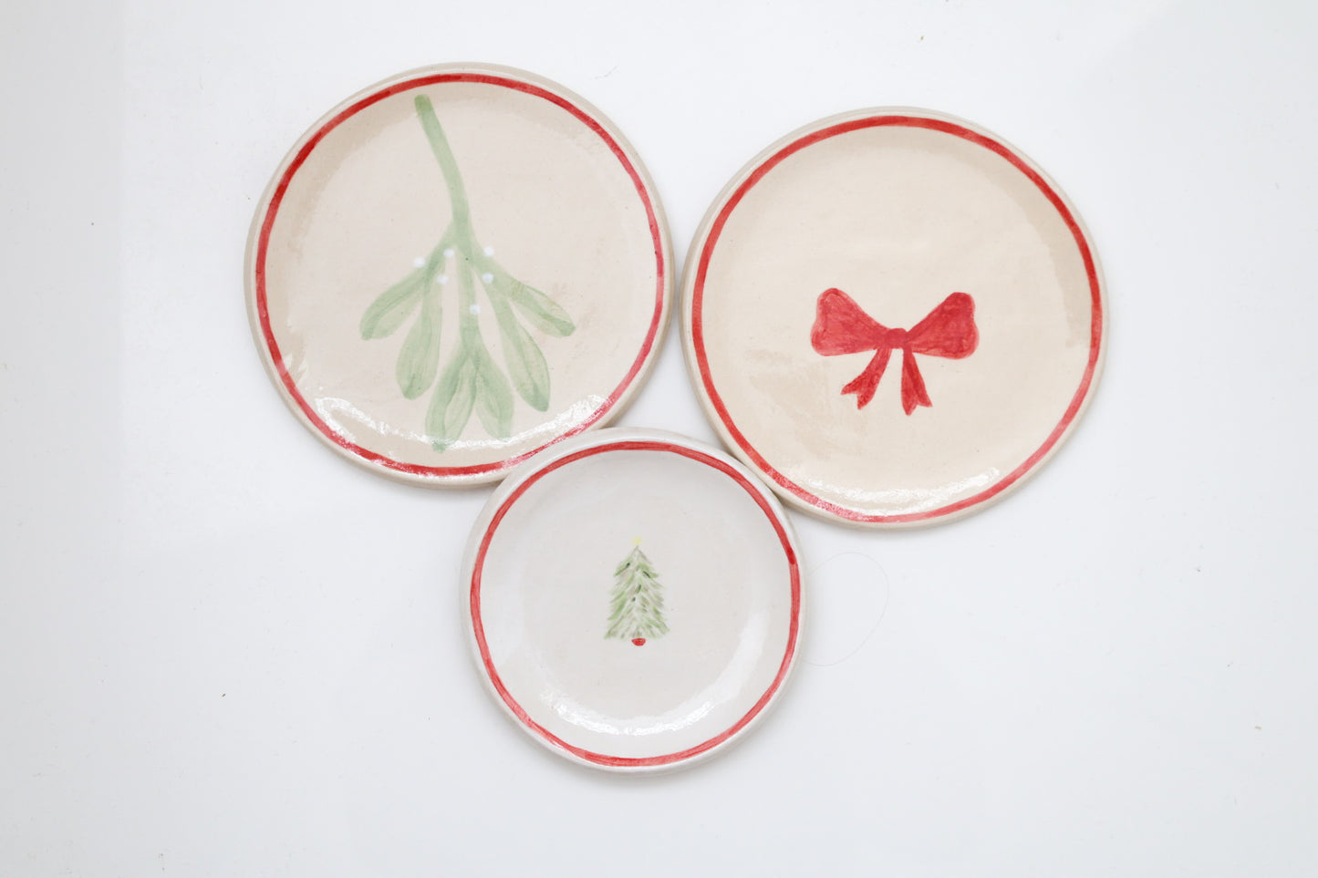 Three ceramic stoneware plates with Christmas-themed designs. Handmade, hand-painted, mistletoe, bow, Christmas tree, Sea Bramble Ceramics. Decorative plates.