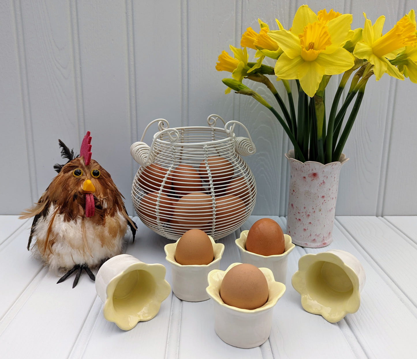 Sea Bramble Ceramics - Handmade Earthenware Daisy egg cups with a scalloped top and glazed with a white exterior and yellow interior. Shown here with eggs, egg basket and a beautiful bunch of daffodils in a red speckled Sea Bramble Daisy vase.