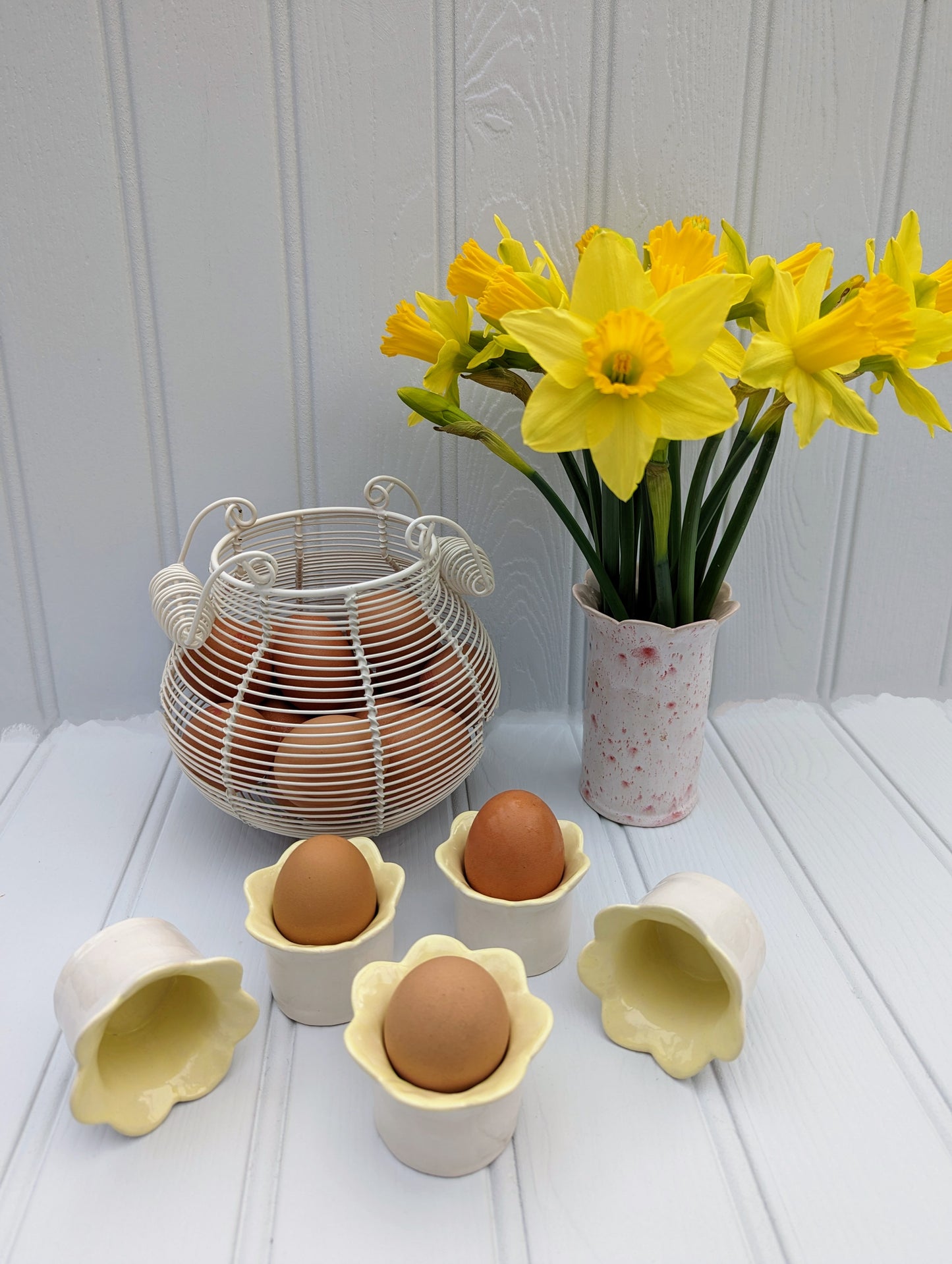 Sea Bramble Ceramics - Handmade Earthenware Daisy egg cups with a scalloped top and glazed with a white exterior and yellow interior. Shown here with eggs, egg basket and a beautiful bunch of daffodils in a red speckled Sea Bramble Daisy vase.