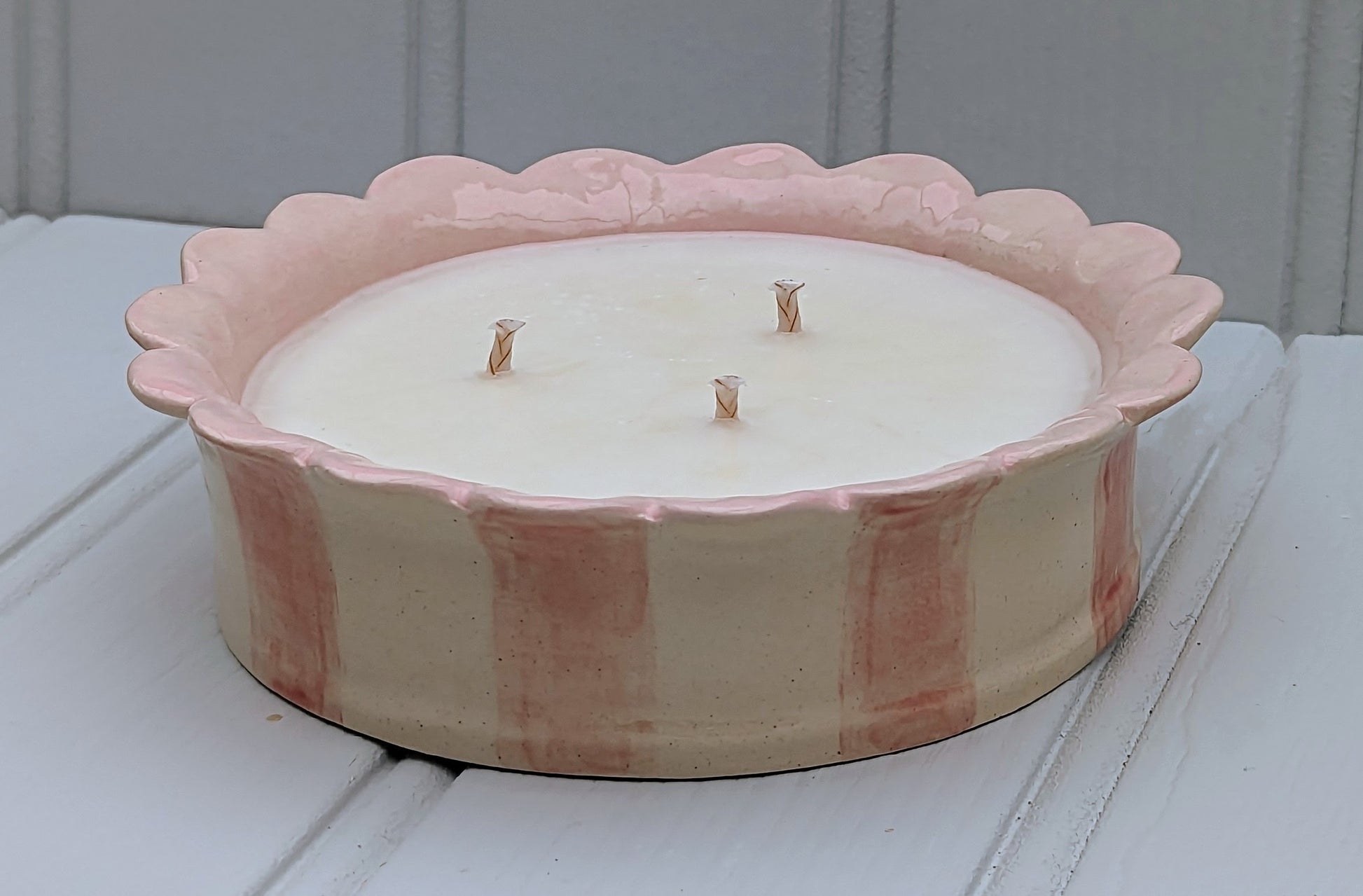 A 3 wick candle in a pink striped ceramic scalloped edge candle holder