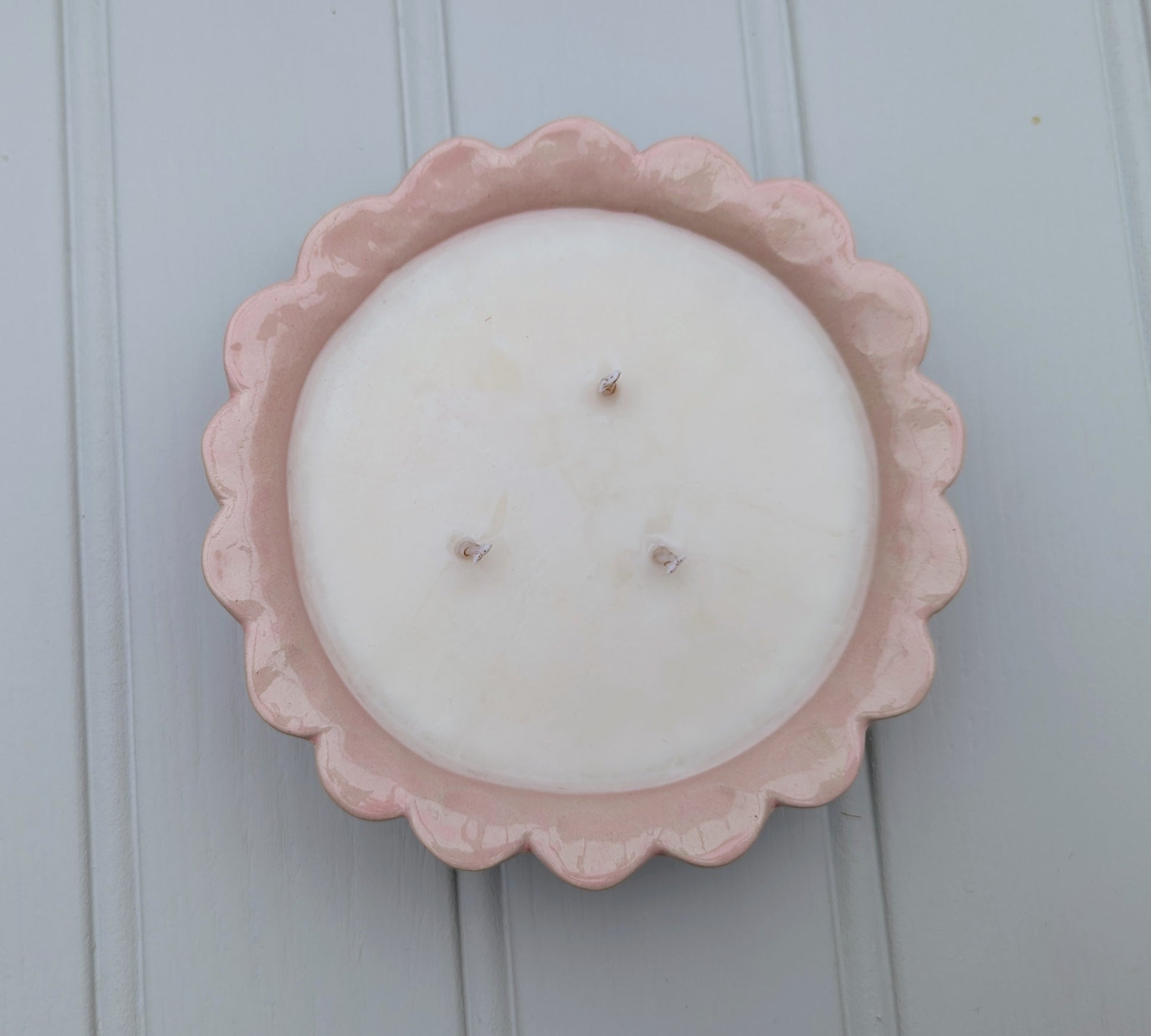 A 3 wick candle in a pink striped ceramic scalloped edge candle holder