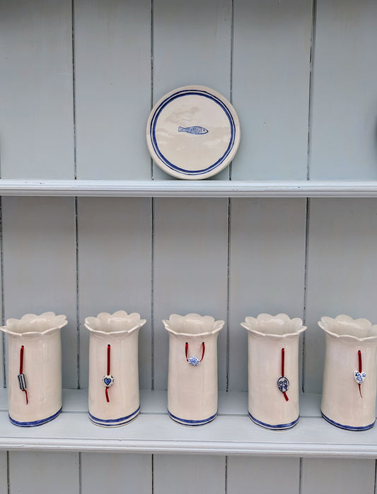 Nautical blue and white ceramic daisy vases, each with a red ribbon and a ceramic charm attached. Designed and handmade exclusively by Sea Bramble Ceramics.