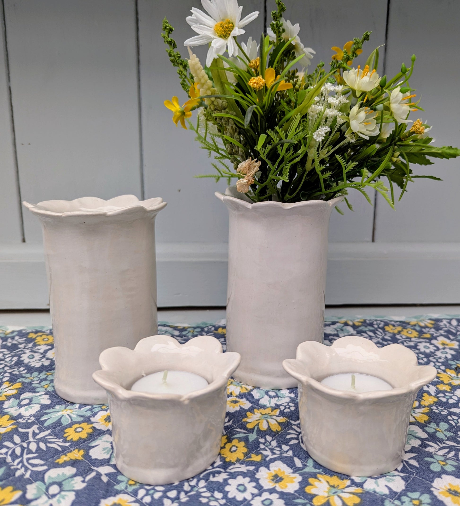 Two white tea light holders by Sea Bramble Ceramics with two white daisy vases in the background..